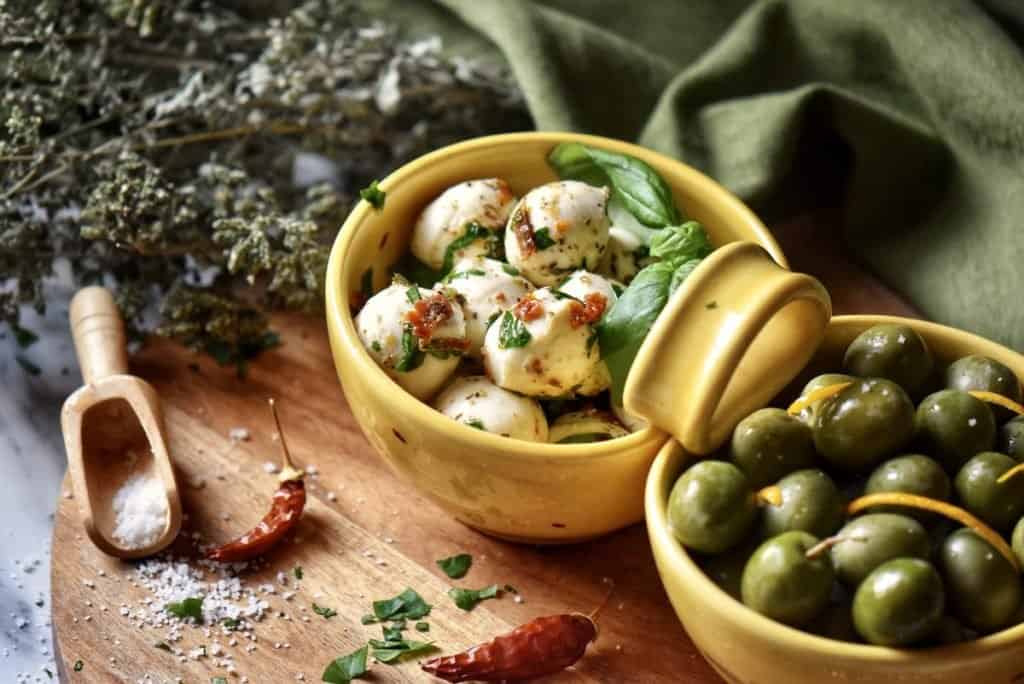Marinated mozzarella balls aka Bocconcini, in a ceramic dish alongside some marinated olives.