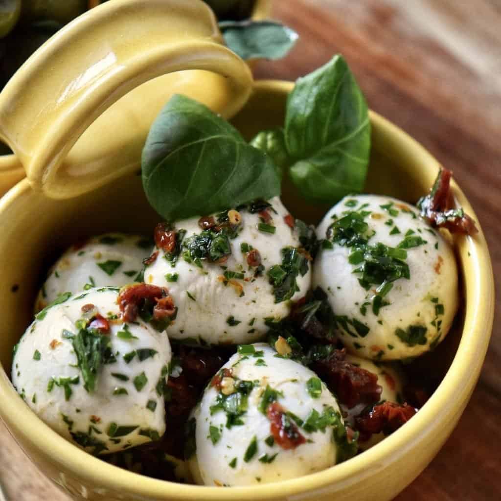 An close up photo of the mozzarella balls aka bocconcini, in a ceramic dish. placed on a wooden board.