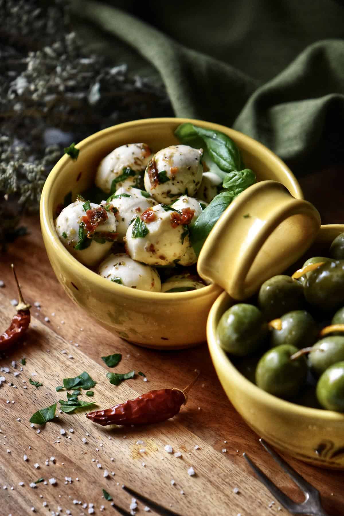 Marinated mozzarella balls aka Bocconcini, in a ceramic dish alongside some marinated olives.
