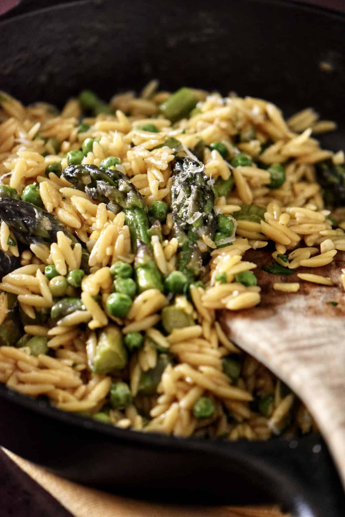 Orzo risotto combined with spring peas and asparagus in a pan.