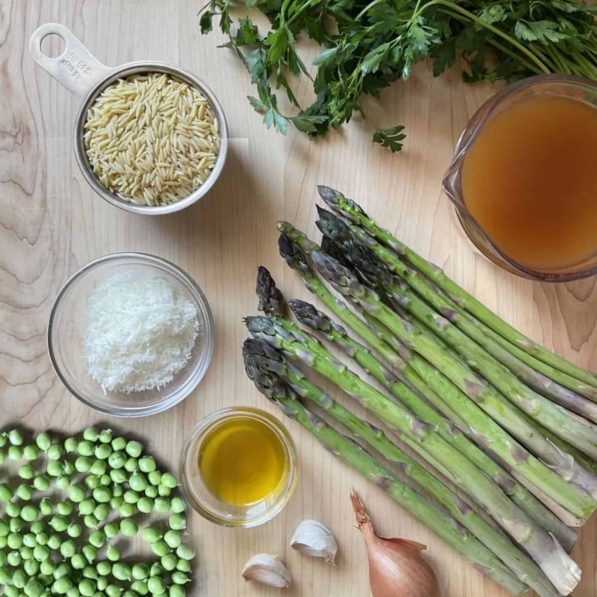 Ingredients to make asparagus orzo risotto on a wooden board.