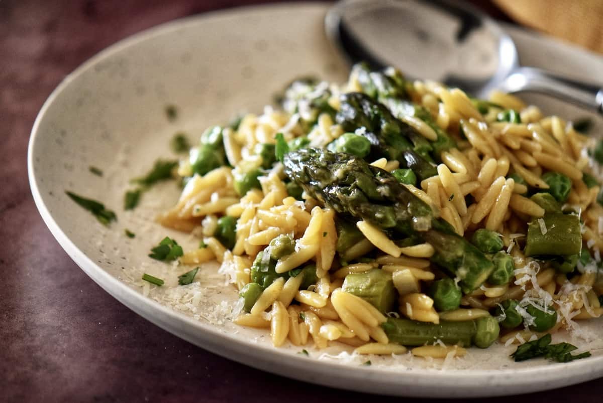 Orzo risotto on a plate garnished with fresh Italian parsley and grated cheese.