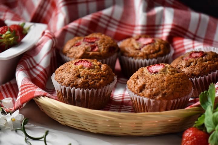 Banana muffins in a wicker basket surrounded by fresh strawberries.