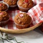 Strawberry muffins placed on a checkered red tea towel, in a wicker basket.