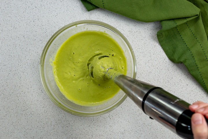 A hand held blender is used to make an asparagus puree.