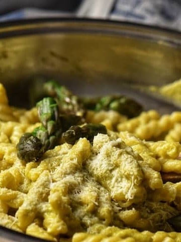 Asparagus tips and pasta in a pan, topped with grated cheese.
