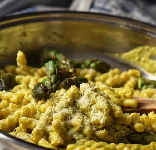 Asparagus tips and pasta in a pan, topped with grated cheese.