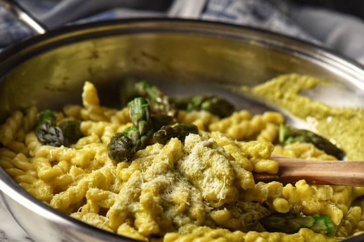 Asparagus tips and pasta in a pan, topped with grated cheese.