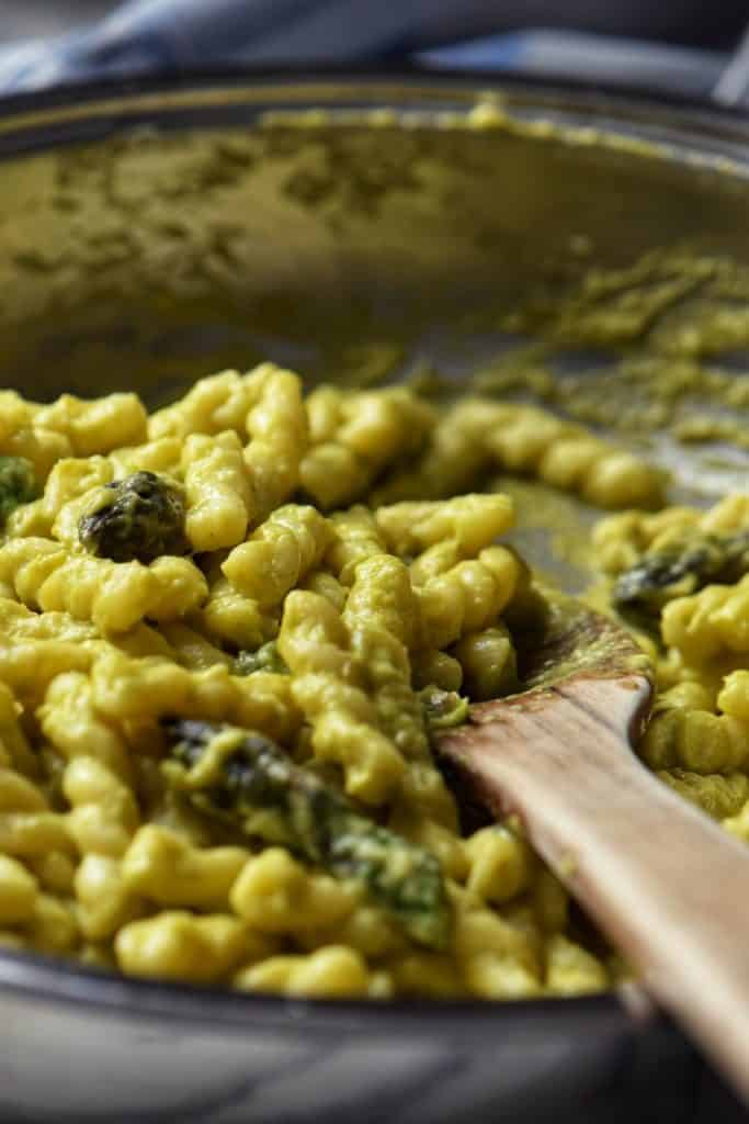 Gemelli pasta being tossed with the creamy asparagus sauce in a pan.