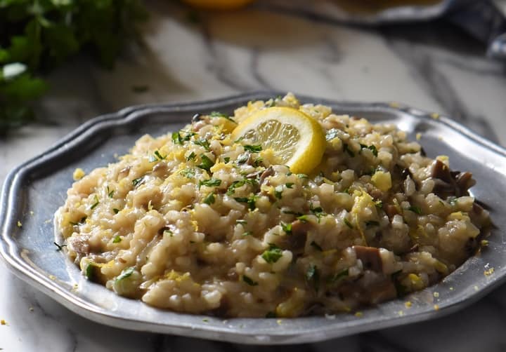 Creamy Mushroom Risotto in a pewter plate topped with lemon zest and a slice of lemon.