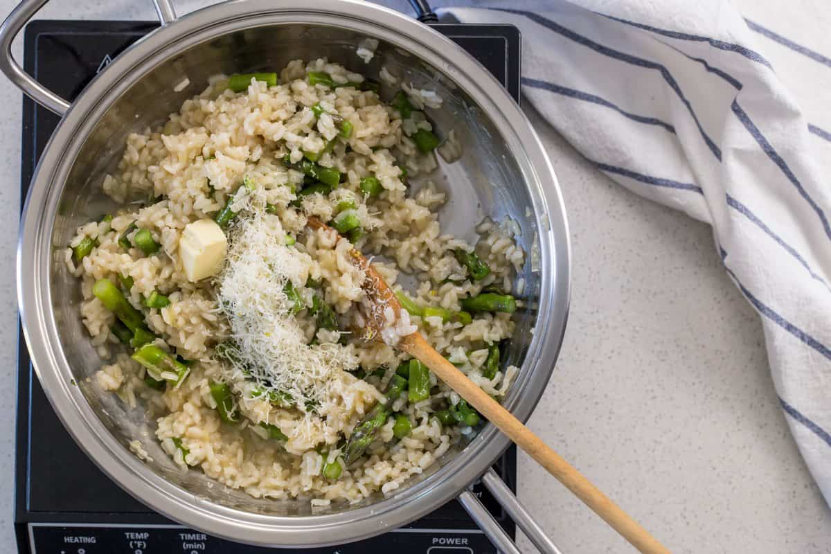 The addition of cheese and butter to a pot of asparagus risotto.