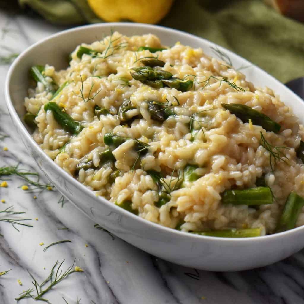 Asparagus risotto in a white oval bowl, set next to a large spoon, ready to be served.