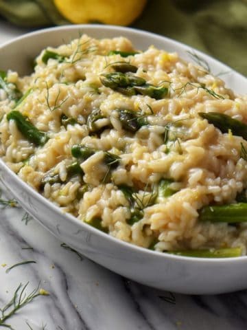 Asparagus risotto in a white oval bowl, set next to a large spoon, ready to be served.