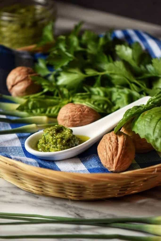 One tablespoon of Garlic Scape Pesto placed in a wicker basket along side walnuts, basil and parsley.