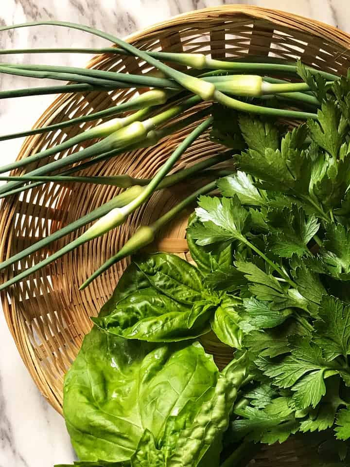 A wicker basket wit garlic scapes, fresh basil and parsley.