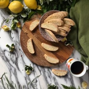 Biscotti scattered on a wooden board, surrounded by fresh lemons and a cup of coffee.