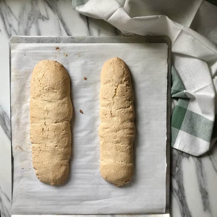 Two freshly baked biscotti loaves on a parchment lined baking sheet.