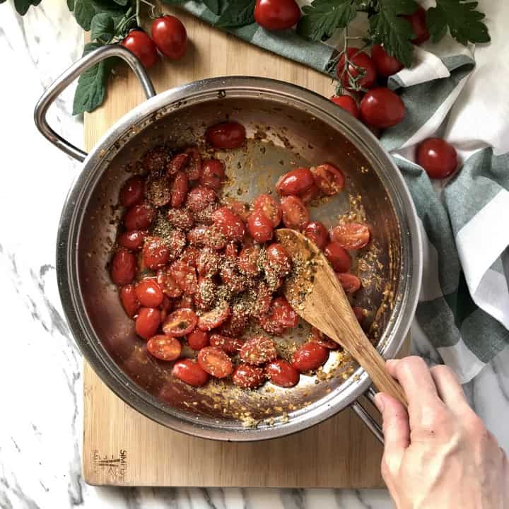 Oregano is combined with a mixture of cherry tomatoes in a large pan.