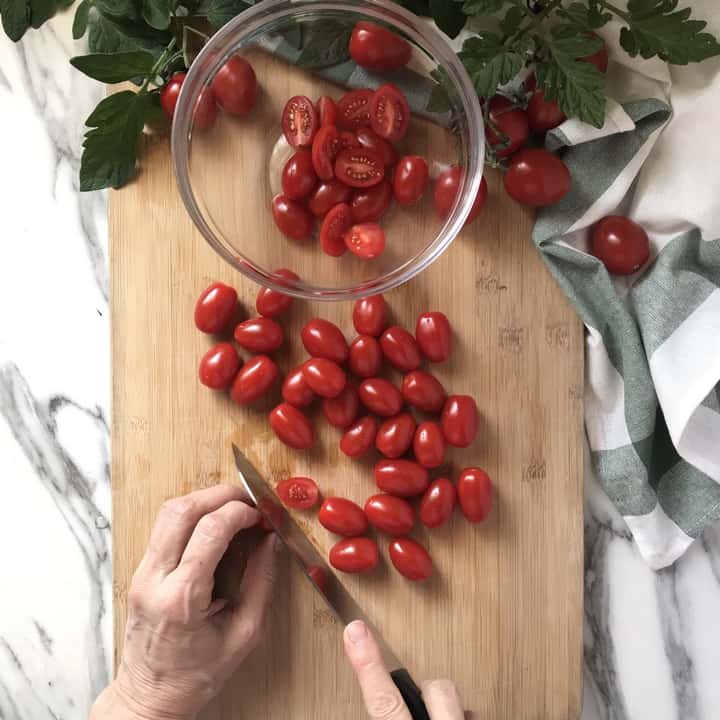 Cherry tomatoes being sliced in half on a wooden board.