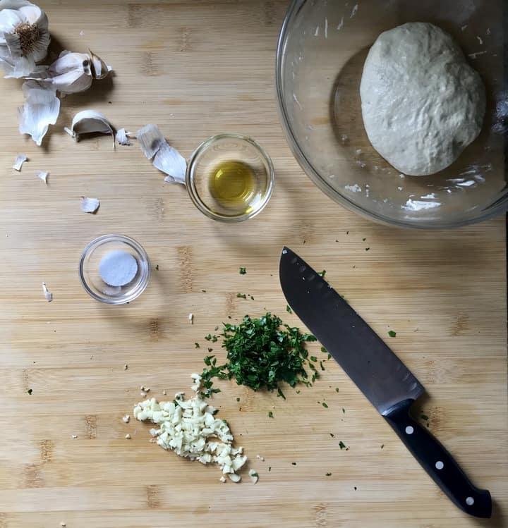 Chopped garlic and parsley on a wooden board. next to a knife.