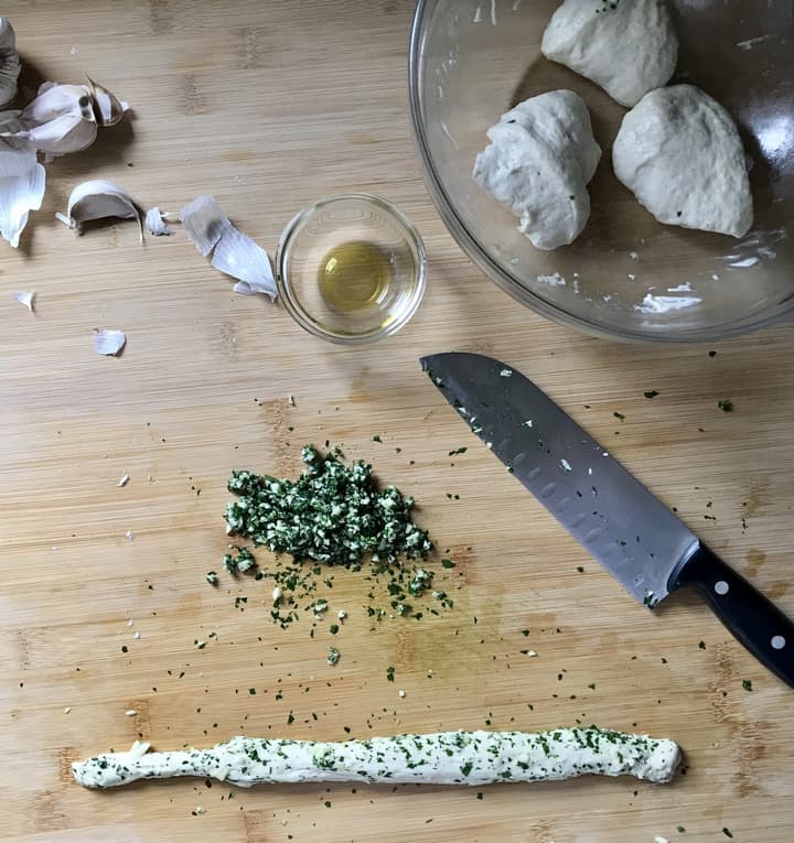 The pizza dough is rolled into the garlic parsley mixture.