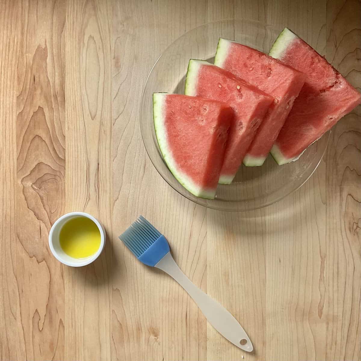 Watermelon wedges next to a small bowl of olive oil.