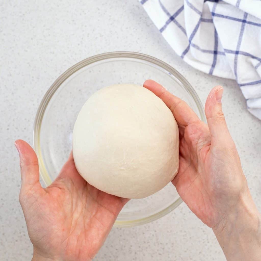 The pizza dough is removed from the stand mixture and is formed into a round ball.