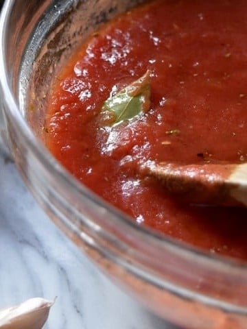A wooden spoon stirring homemade pizza sauce.