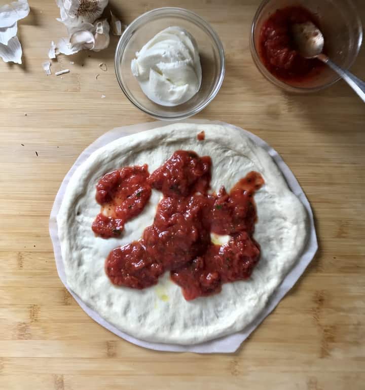Pizza sauce being spread over pizza dough.