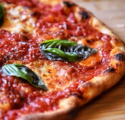 Basil leaves garnish a freshly grilled Italian pizza.