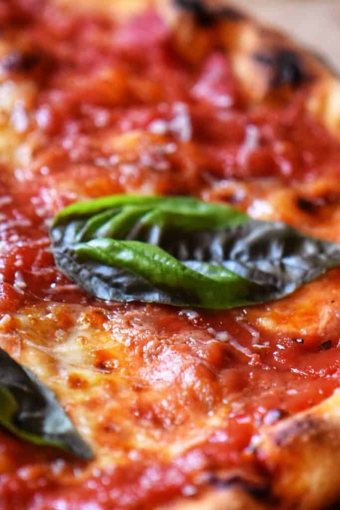 A close up of a basil leave atop a slice of margherita pizza. 