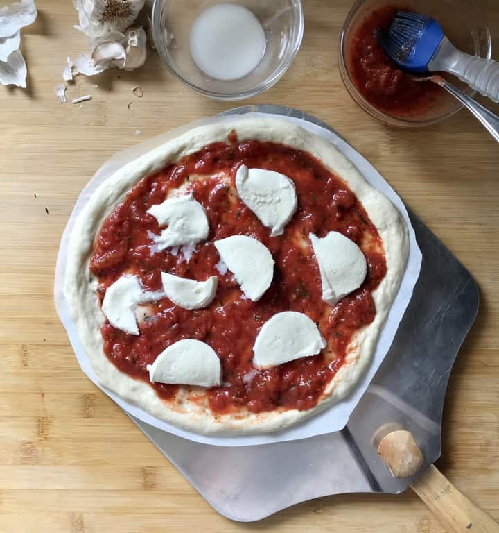 A pizza paddle is used to lift the Margherita pizza from the wooden board.