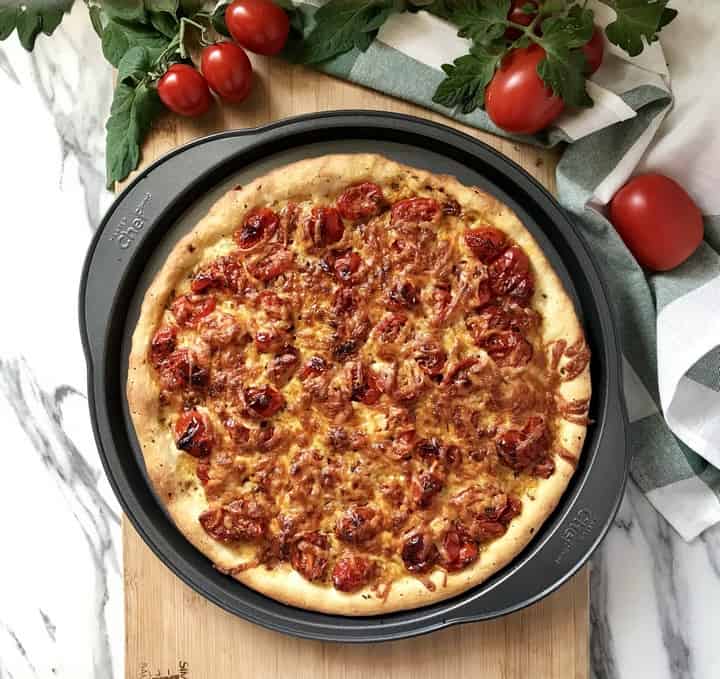 A pesto pizza freshly baked in a round pizza pan.