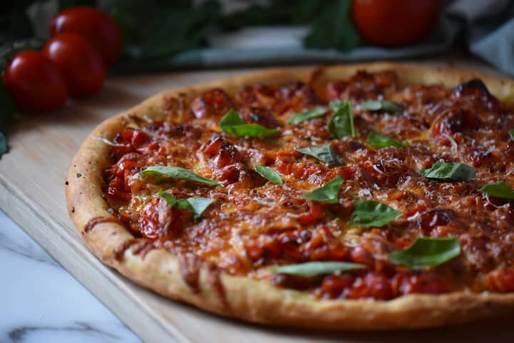 A freshly made pizza with cherry tomatoes and pesto, fresh out of the oven.