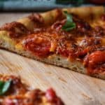 Cherry tomatoes top this pesto pizza that is on a wooden board.