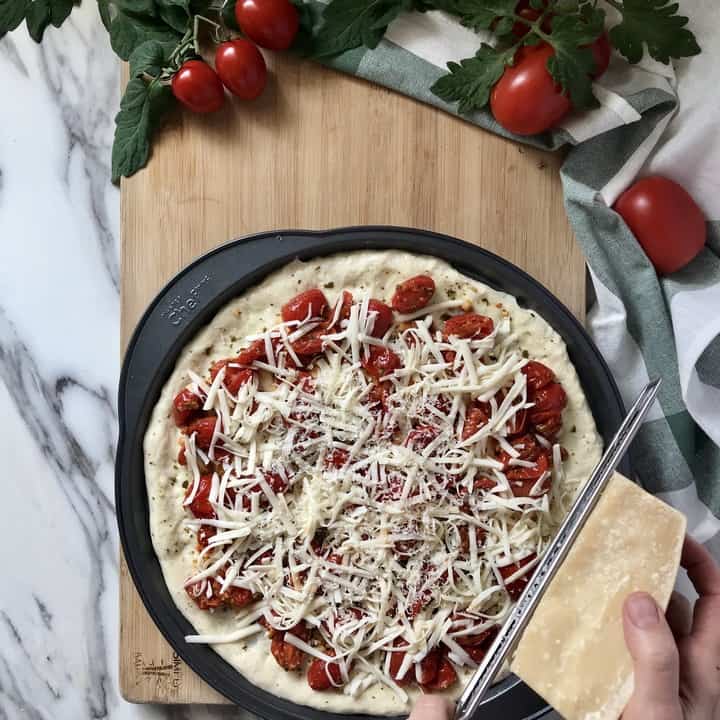 Parmigiana Reggiano cheese being grated over the top of the pesto pizza before baking.