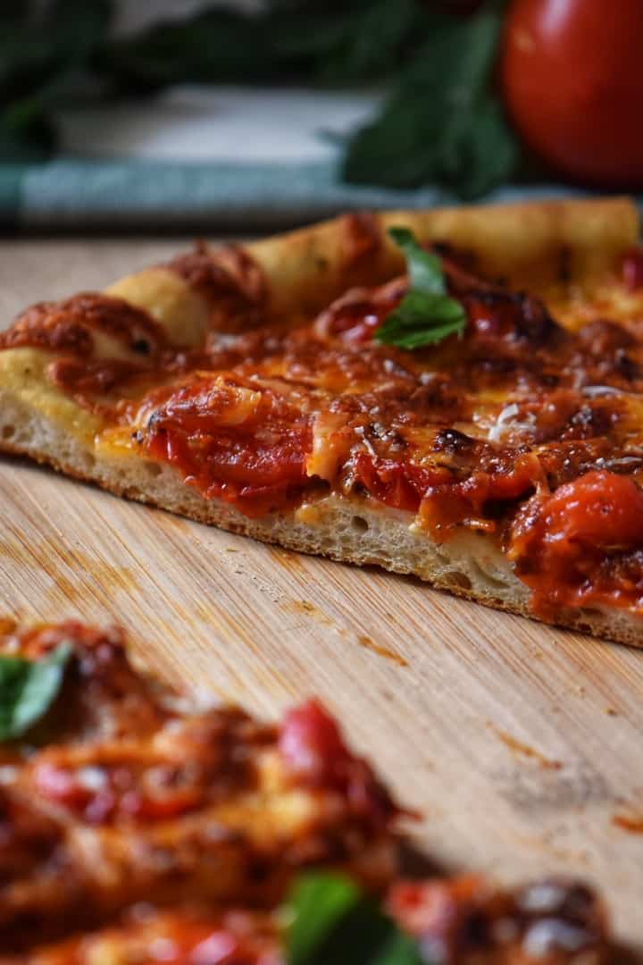 A slice of pesto pizza on a wooden board.