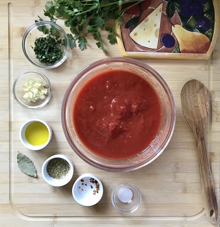 A bowl of hand crushed San Marzano tomatoes surrounded by pizza sauce ingredients.