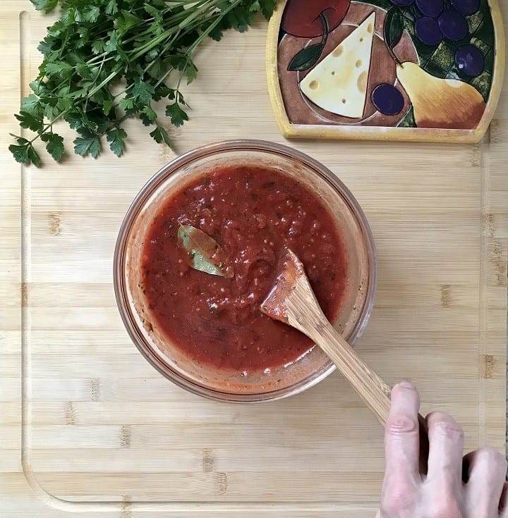 A bay leaf is being removed from the homemade pizza sauce.