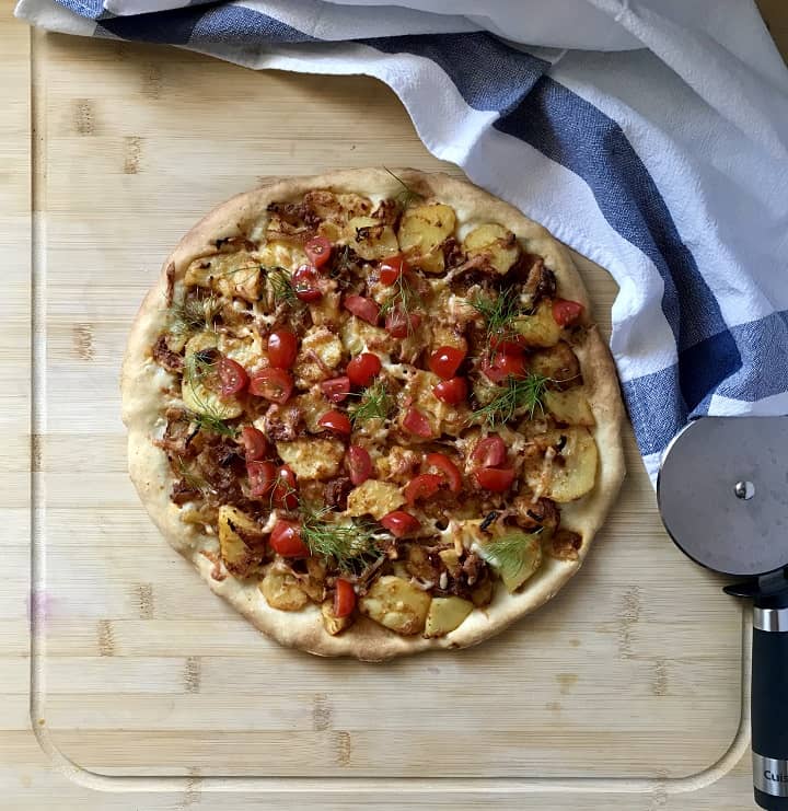 A potato pizza garnished with chopped fresh tomato and fennel fronds.