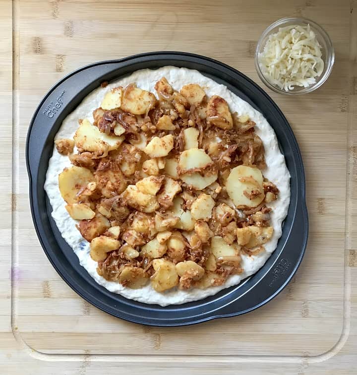 A potato pizza in a pizza pan ready to be baked.