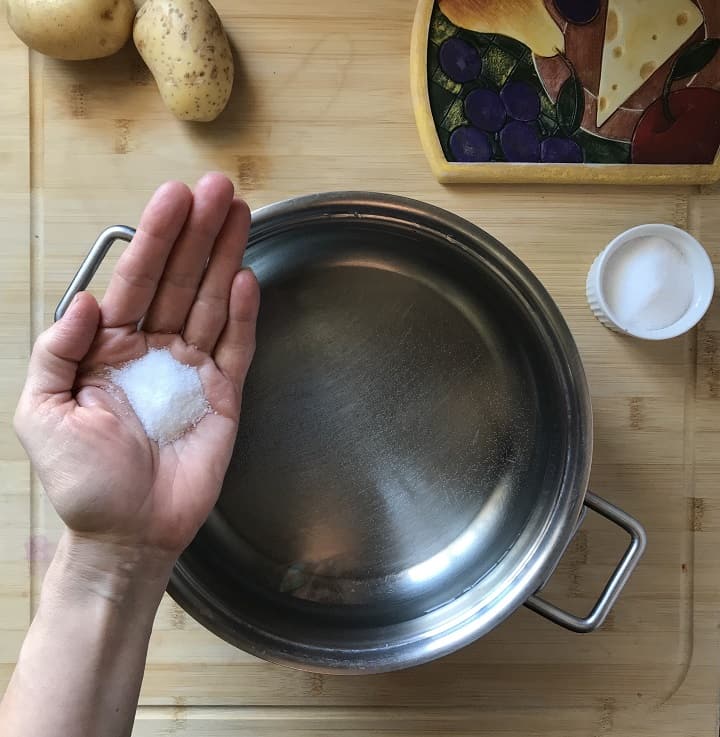A tablespoon of salt being added to a pot of water.