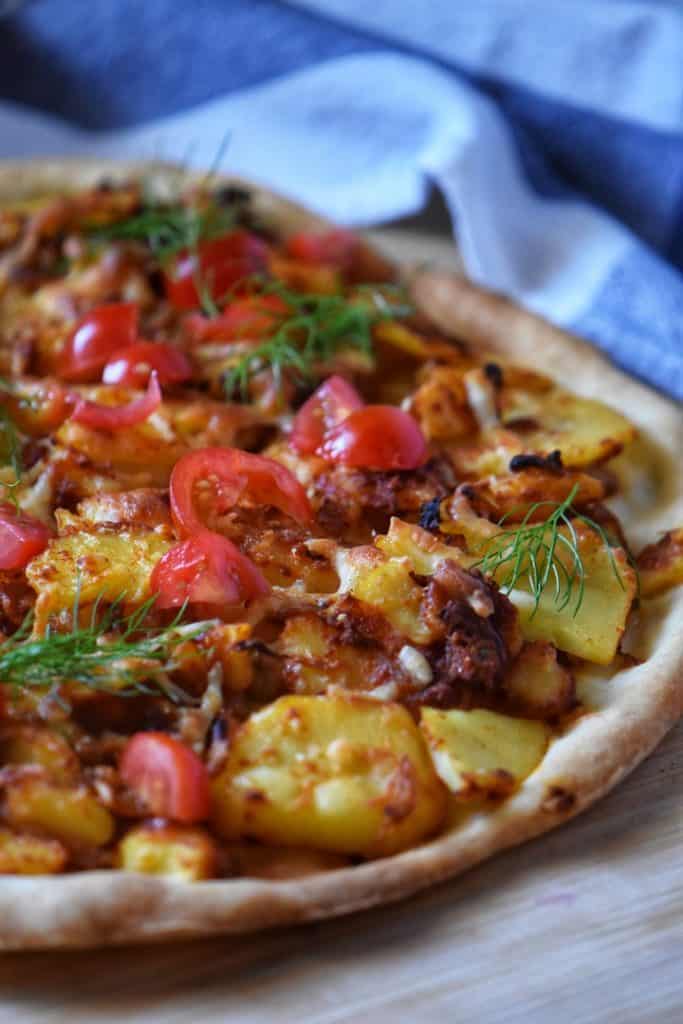 A potato pizza topped with chopped tomatoes and garnished with dill.