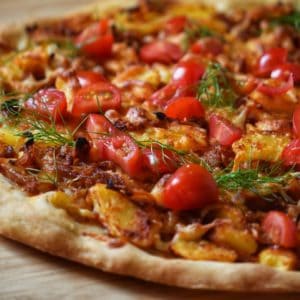 A potato pizza topped with grated cheese, chopped tomato and dill.