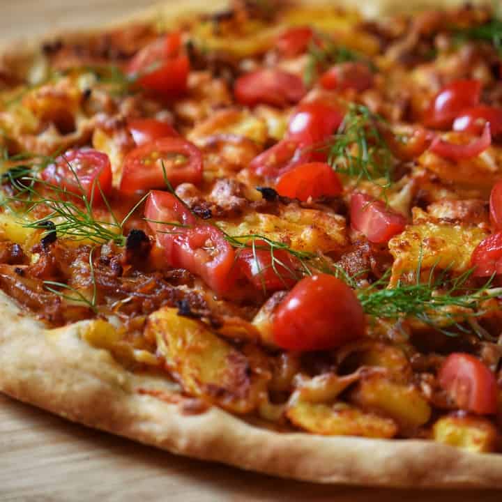 A potato pizza topped with grated cheese, chopped tomato and dill.