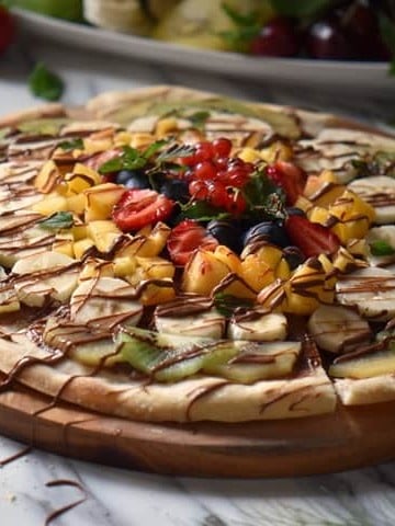 A pizza topped with fresh fruit on a wooden serving board.