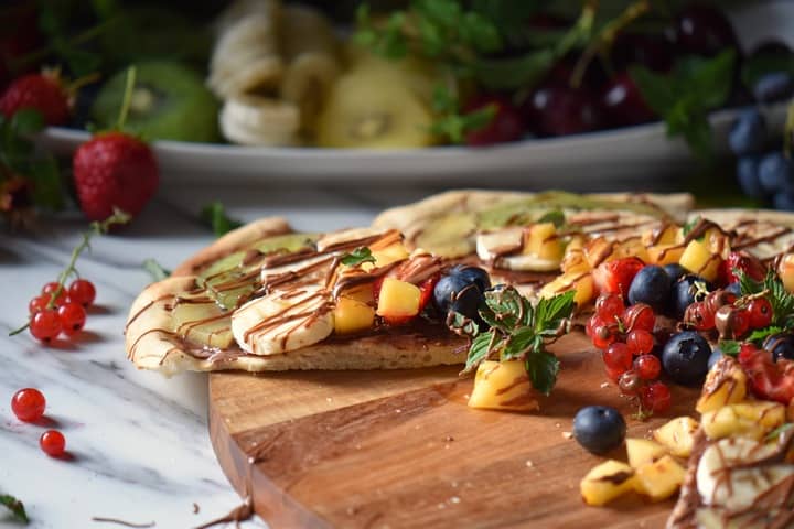 A fruit topped pizza on a wooden board.