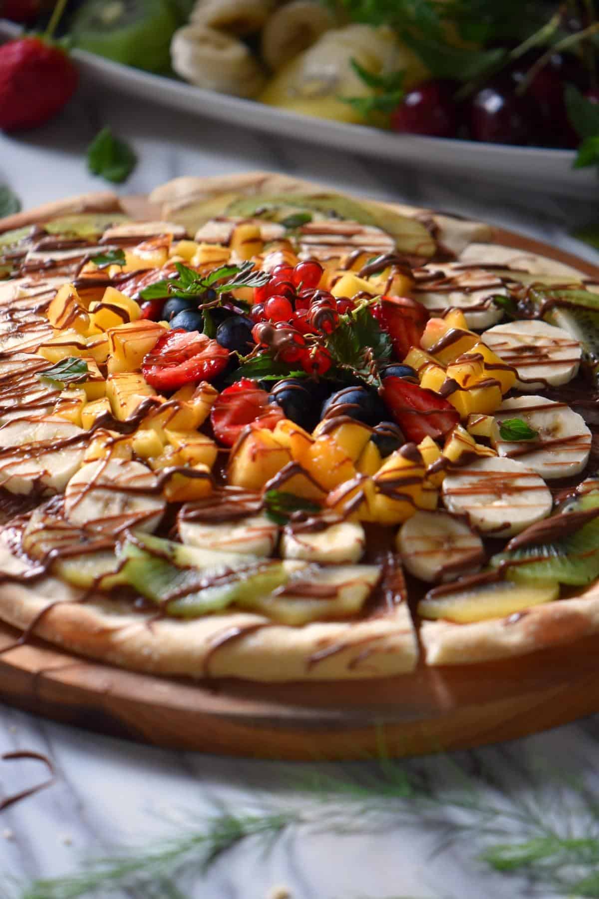 A thin pizza crust topped with seasonal fruits that have been drizzled with chocolate.
