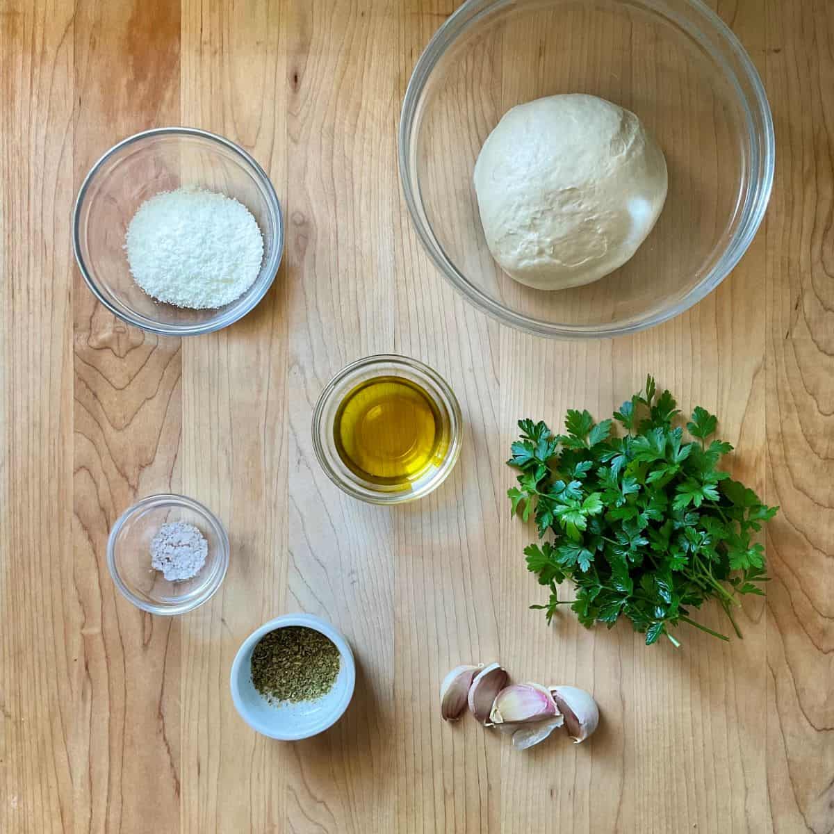 Ingredients to make garlic knots with pizza dough on a wooden board.