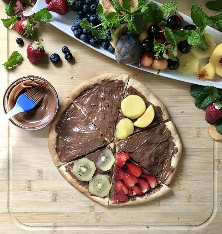 Fresh fruit being placed on a chocolate covered pizza crust.